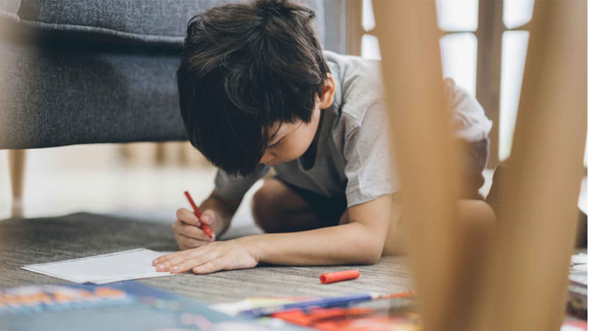 Imagem de um menino no chão com a cabeça abaixada, com um papel e uma canetinha em suas mãos