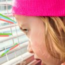 Imagem do rosto de uma criança com uma touca rosa com o olhar concentrado para janela e alguns grafismos coloridos perto dos seus olhos.