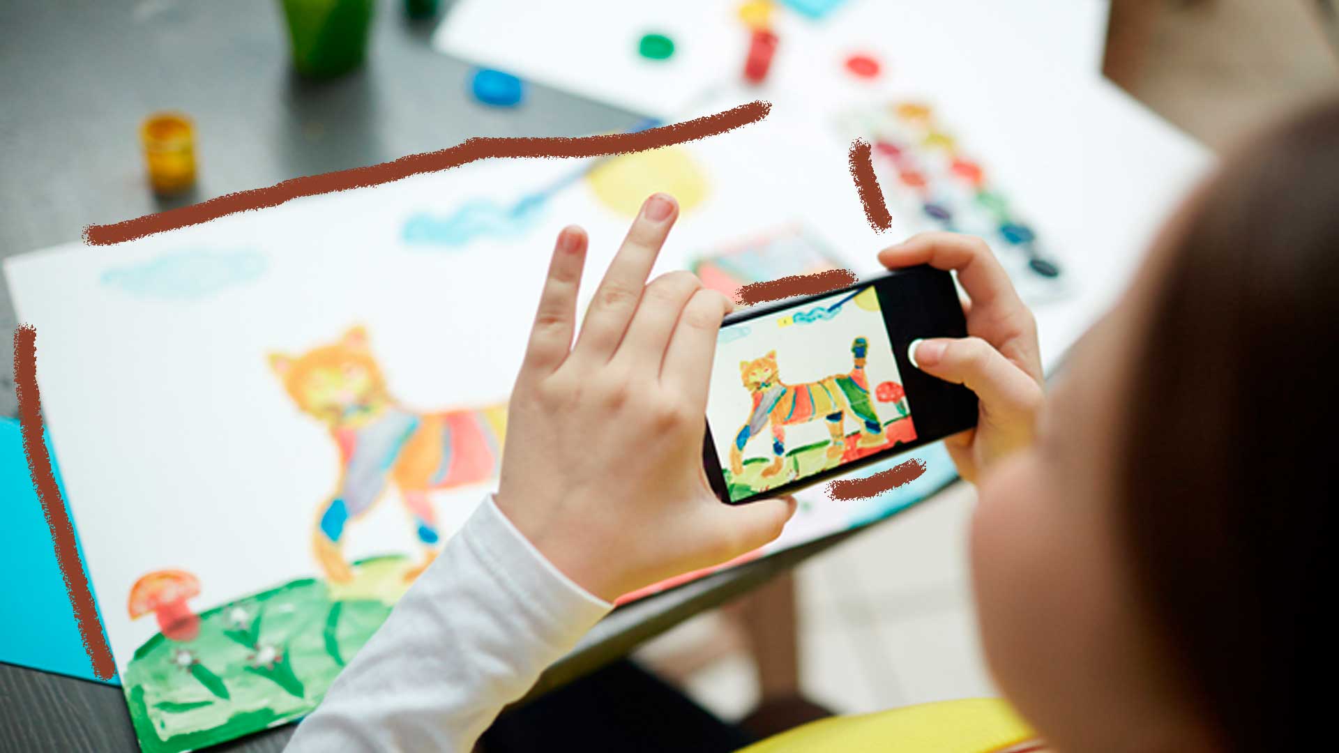 Imagem da mão de uma criança com o celular em mãos tirando foto do desenho de um leão