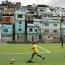 Imagem de uma quadra de futebol em uma favela para representar experiências comunitárias. Um menino negro está jogando bola