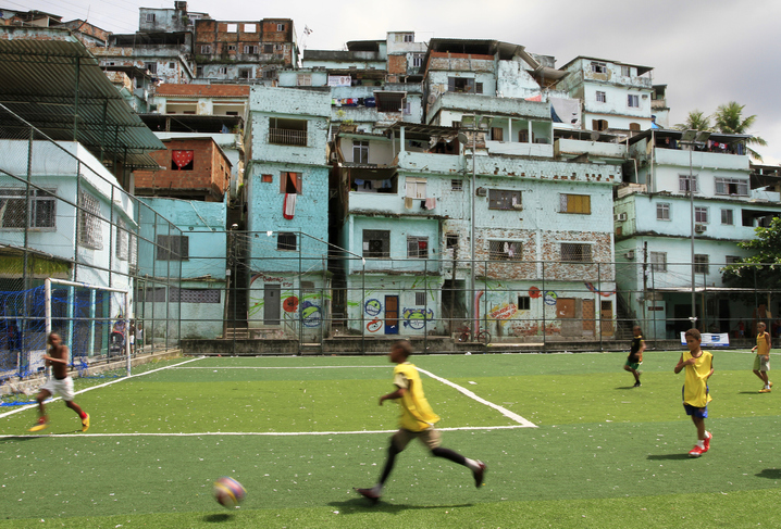 Imagem de uma quadra de futebol em uma favela para representar experiências comunitárias. Um menino negro está jogando bola