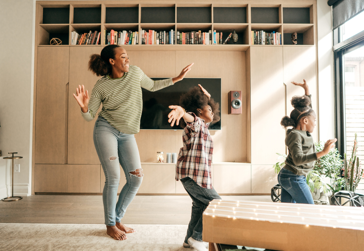 Imagem de uma mãe dançando com sua filha e seu filho na sala de estar.