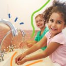 Imagem de uma menina e um menino lavando as mãos na pia do banheiro e sorrindo