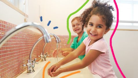Imagem de uma menina e um menino lavando as mãos na pia do banheiro e sorrindo