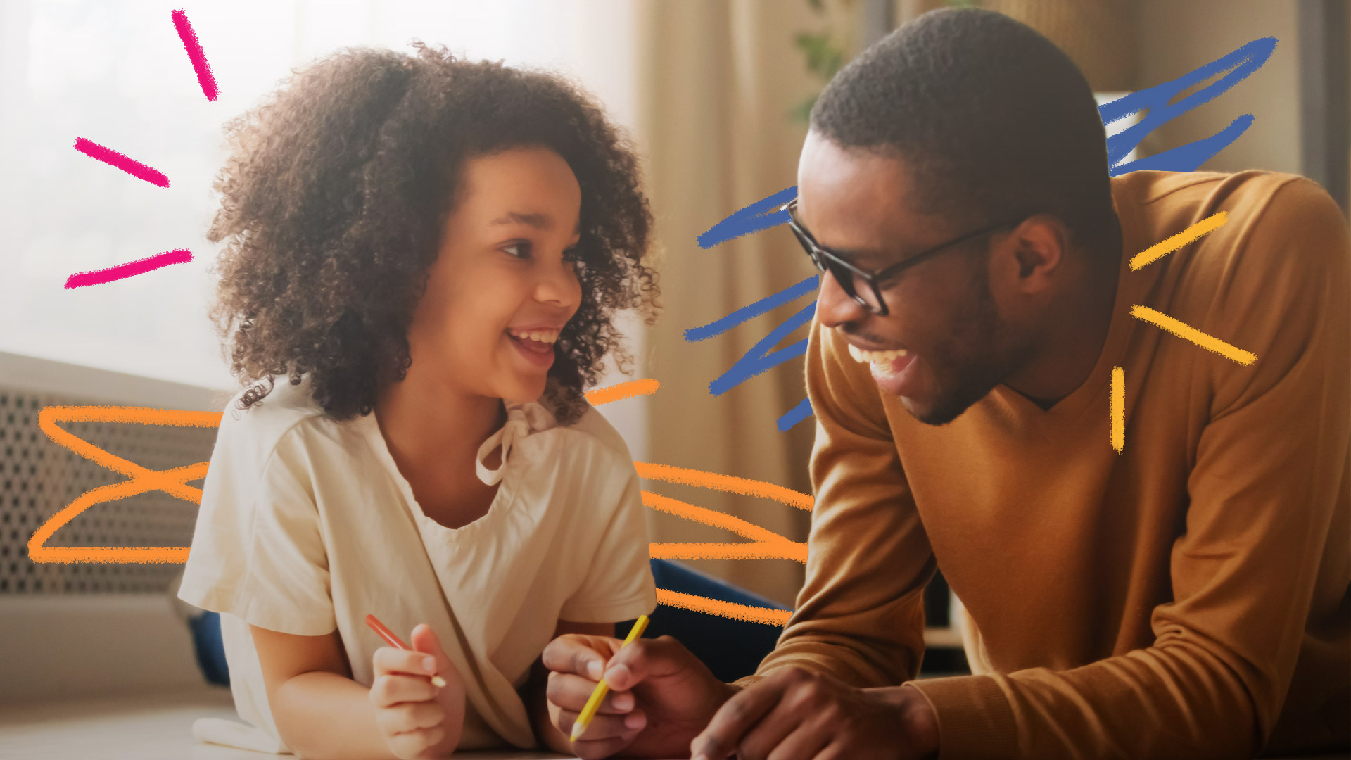 Imagem de pai e filha negros deitados no chão. Eles estão sorrindo e desenhando com lápis colorido em um caderno.