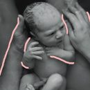 Imagem em preto e branco de um bebê que acabou de nascer. Ele está nas mãos de sua mãe