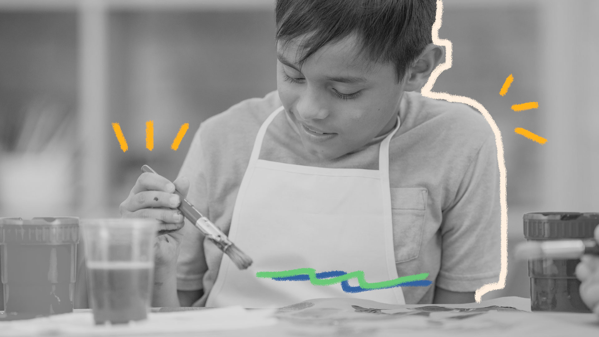 Um menino que aparenta 7 anos de idade, está com um pincel na mão, desenhando em um papel
