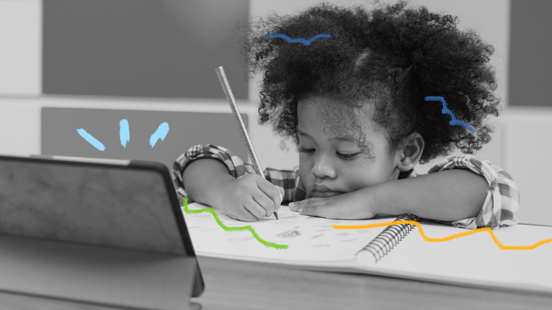 Arte e educação para crianças: uma menina negra se debruça sobre um caderno onde desenha seguindo algum curso ou vídeo por um tablet apoiado na mesa em frente a ela