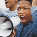 Imagem de uma criança negra empunha um megafone e grita por seus direitos