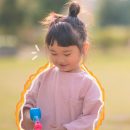 Imagem de uma menina asiática está sorrindo e segurando um brinquedo de plástico, em um parque