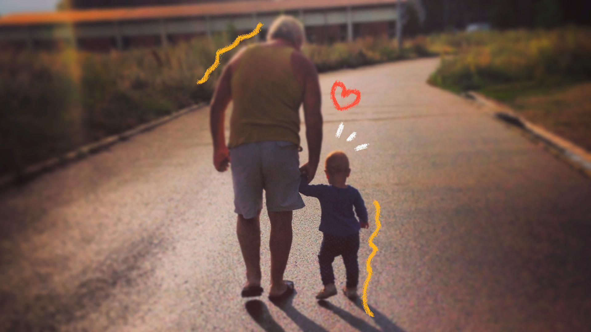 Foto de um avô dando as mãos ao neto bebê acompanhando-o nos primeiros passos e ambos caminham lado a lado, de costas, seguindo por uma estrada