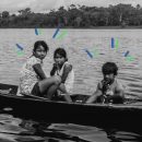 Demarcação de terras indígenas: oto em preto e branco de três crianças indígenas (2 meninas e 1 menino) em uma canoa, dentro de um rio, olhando para a câmera. Vê-se a floresta ao fundo.