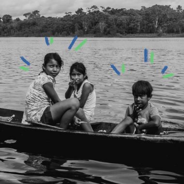 Demarcação de terras indígenas: oto em preto e branco de três crianças indígenas (2 meninas e 1 menino) em uma canoa, dentro de um rio, olhando para a câmera. Vê-se a floresta ao fundo.