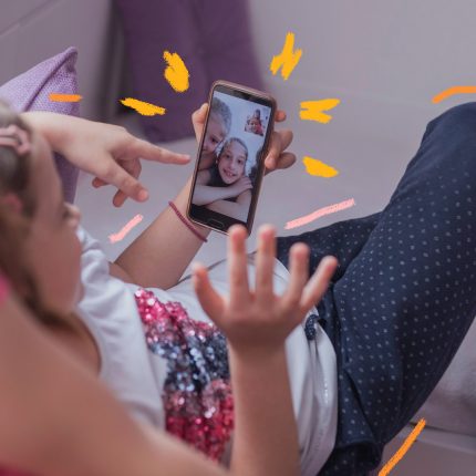 Imagem de uma criança com um celular na mão falando com outras crianças em uma vídeo chamada. Texto sobre convívio social entre crianças durante o confinamento