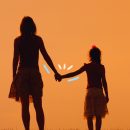 Saúde mental infantil: a silhueta de mãe e filha aparece contra a luz. Elas estão de costas e caminham lado a lado, de mãos dadas.