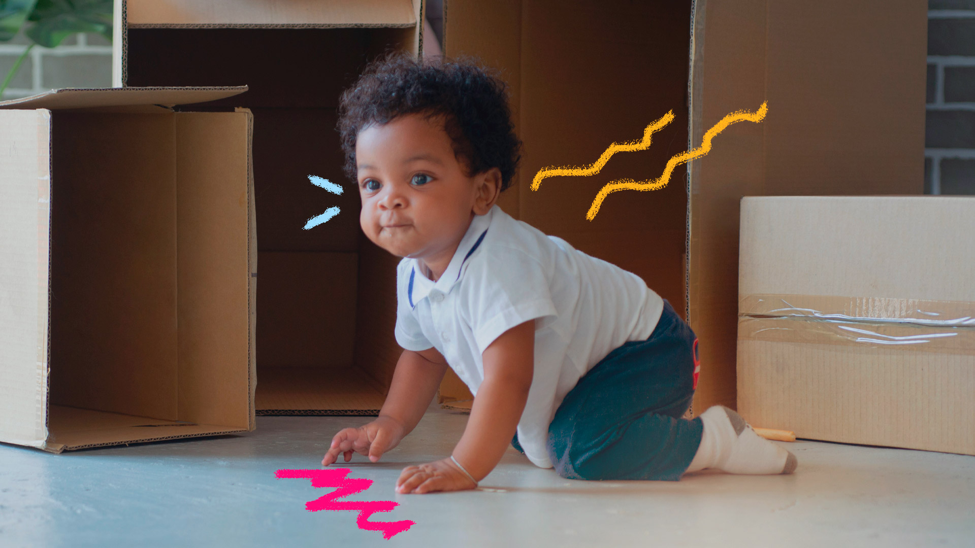 Imagem de um bebê negro engatinhando próximo de caixas de papelão que estão no chão. Ele usa camiseta branca, calça e meias.