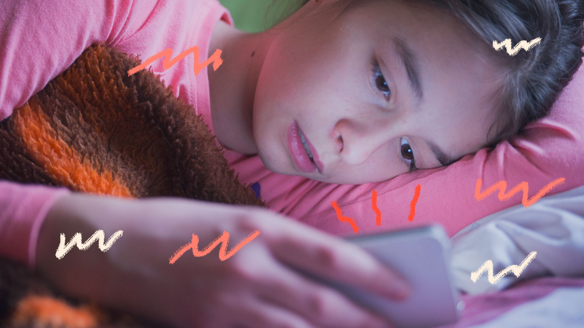 Imagem de uma menina deitada em sua cama olhando para a tela de um celular