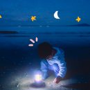 Foto de um menino na praia à noite. Ele brinca com um abajur e ao redor há estrelas e luas desenhadas