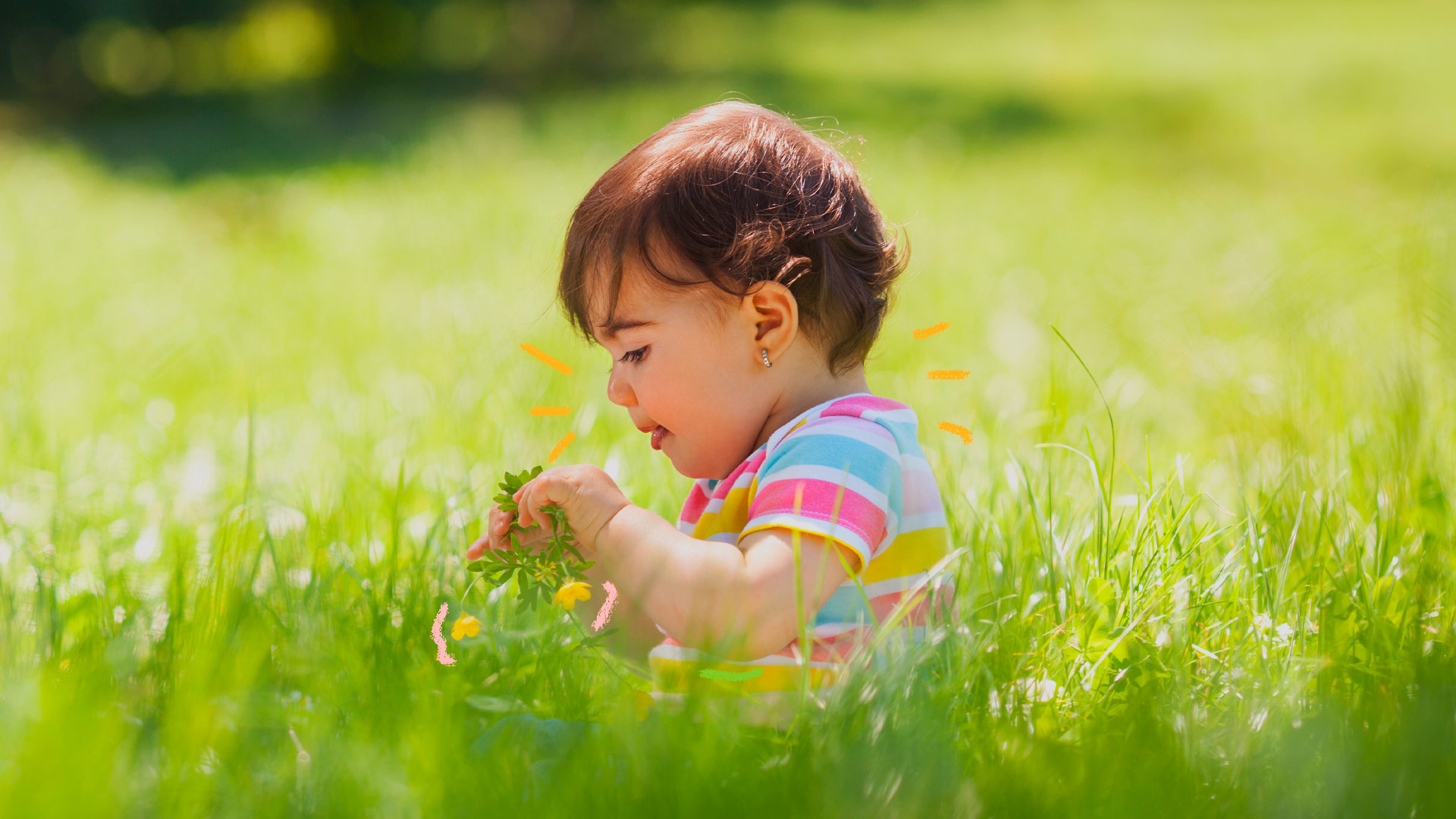 Imagem de uma menina pequena de cabelo curto. Ela brinca com uma flor em meio a um campo verde.