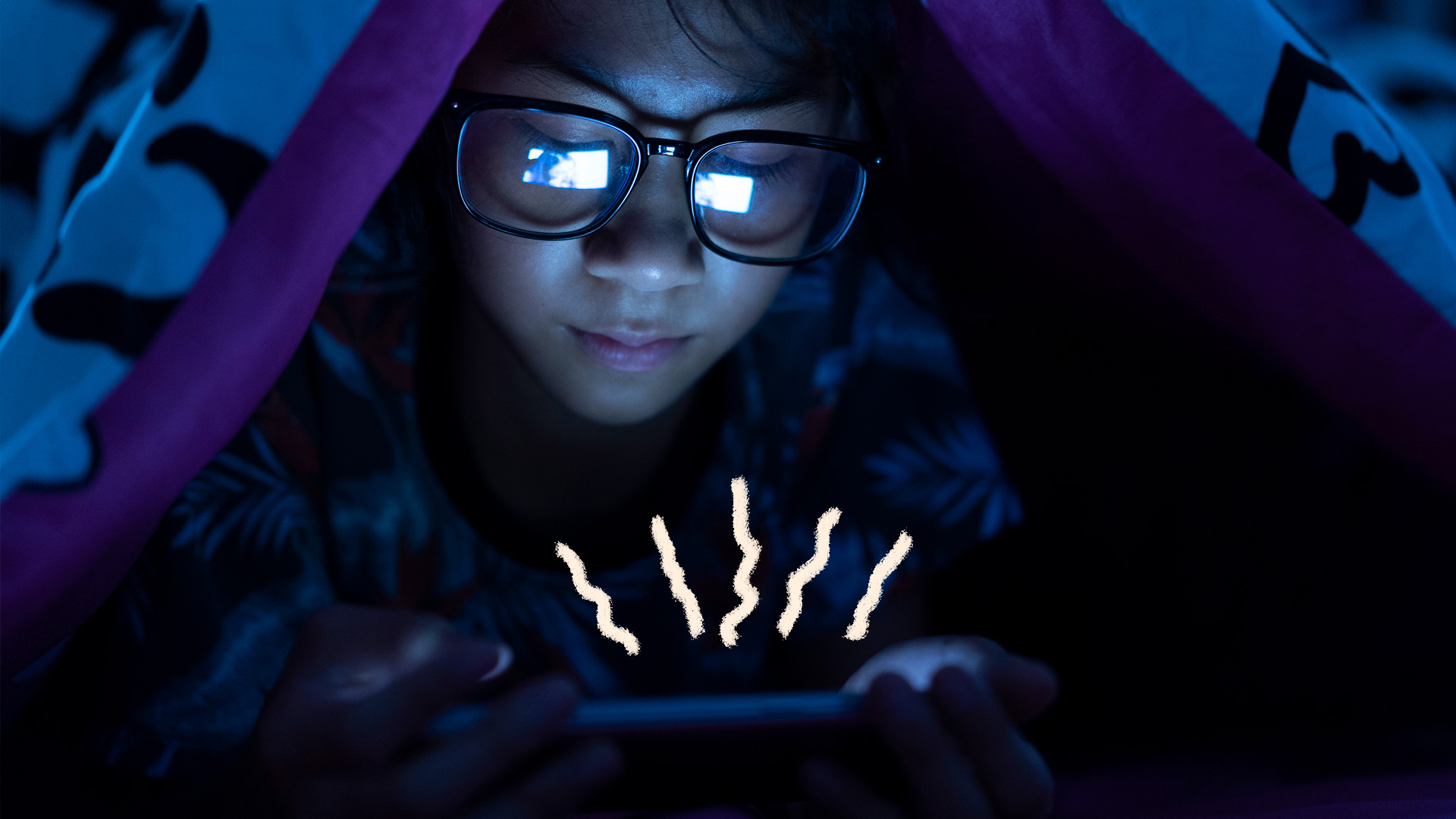 Miopia infantil: um menino usa óculos e olha para a tela de um celular em um ambiente escuro