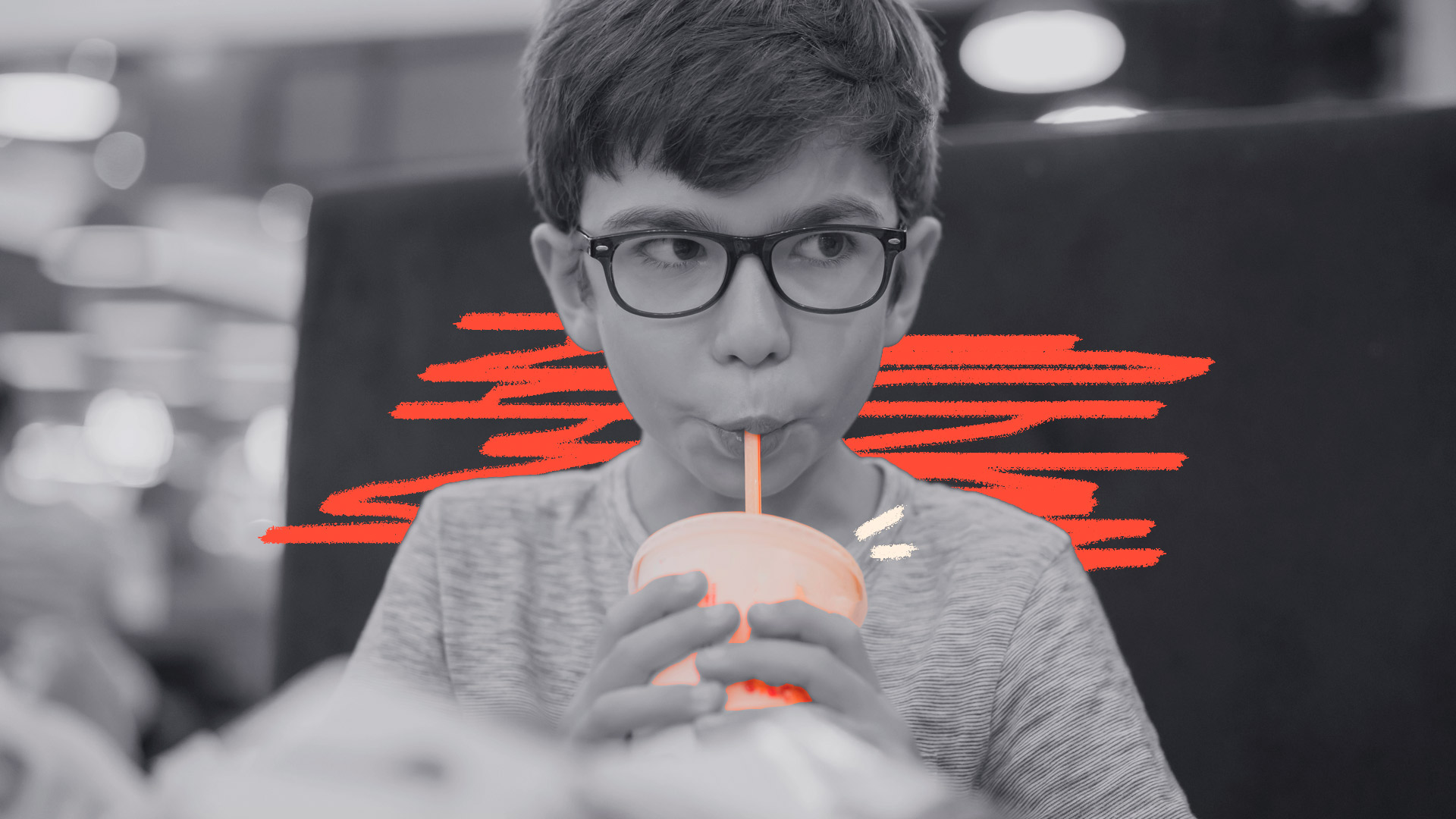 Imagem em preto e branco de um menino, de óculos, tomando uma bebida em um copo plástico com canudinho.