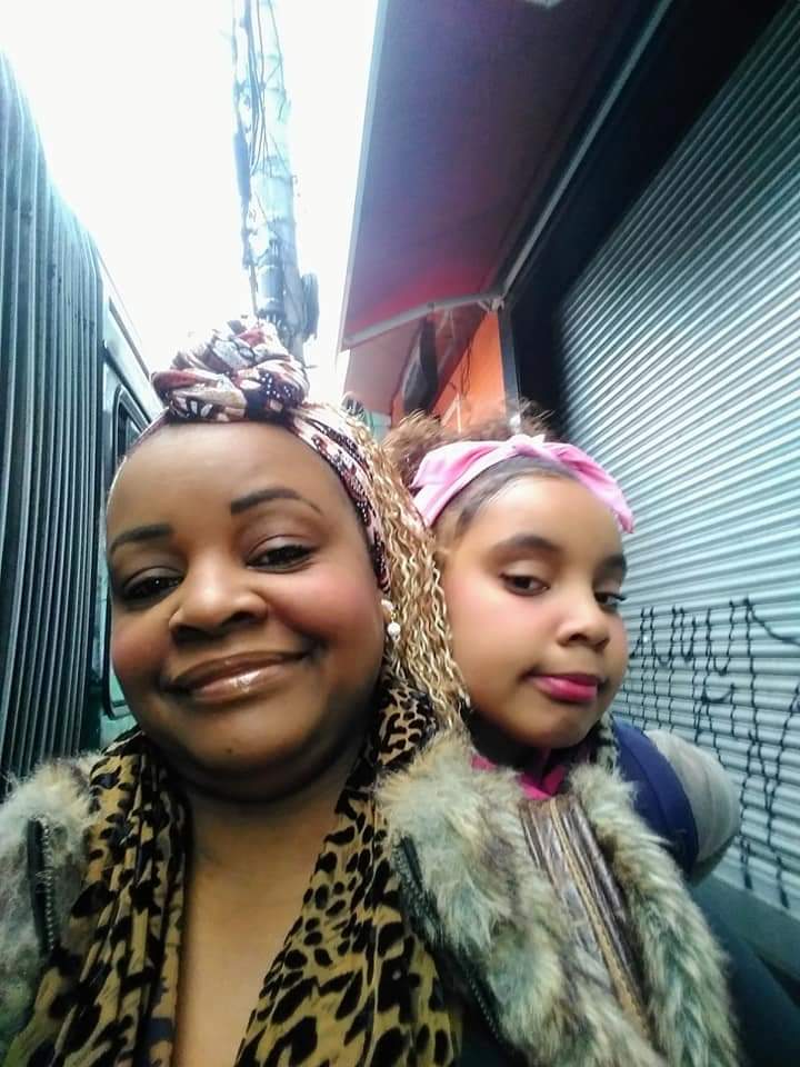Abandono afetivo paterno: Foto de Elizabete com a filha Laila. Uma mulher negra com tranças coloridas faz uma selfie com uma criança negra com faixa rosa no cabelo, posicionada no seu ombro direito.