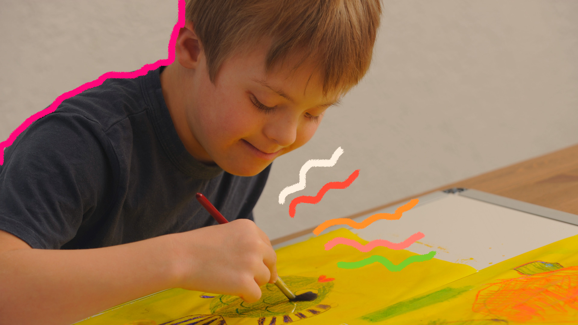 Imagem de um menino em cima da mesa usando pincel e cores em seu desenho
