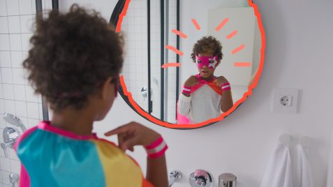 Representatividade negra: um menino vestido com fantasia de super-herói se olha pelo espelho do banheiro