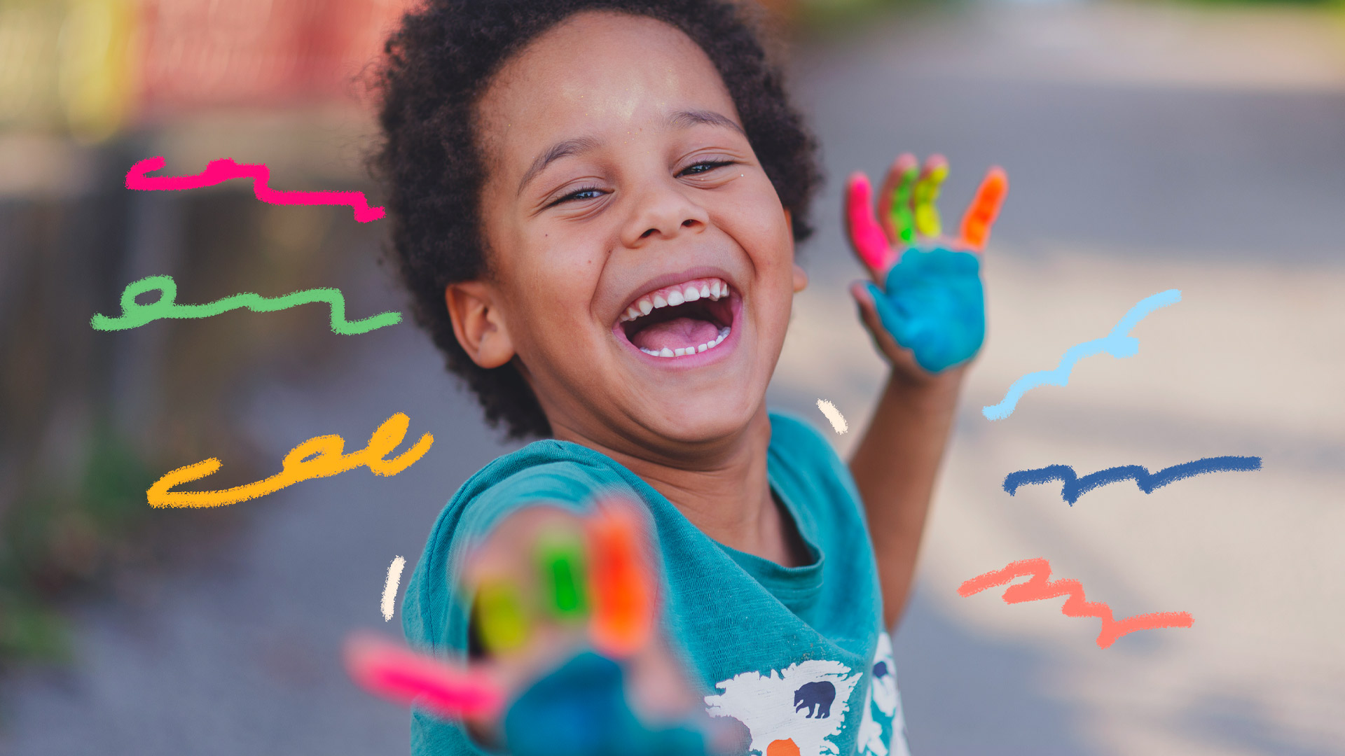 Projetos antirracistas: foto de um menino sorrindo que mostra as duas mãos coloridas com tinta cada dedo com uma cor.