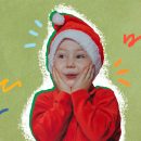 Um menino vestido de vermelho com gorro de Papai Noel está com as duas mãos no rosto