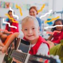 Educação inclusiva: um garoto que tem síndrome de Down aparece em destaque segurando um violão. Ao fundo, em círculo, estão seus colegas e a professora da turma