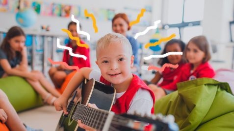 Educação inclusiva: um garoto que tem síndrome de Down aparece em destaque segurando um violão. Ao fundo, em círculo, estão seus colegas e a professora da turma