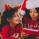 Mãe e filha vestidas de vermelho lêem um livro de Natal. Ao fundo, árvore natalina e embrulhos de presente