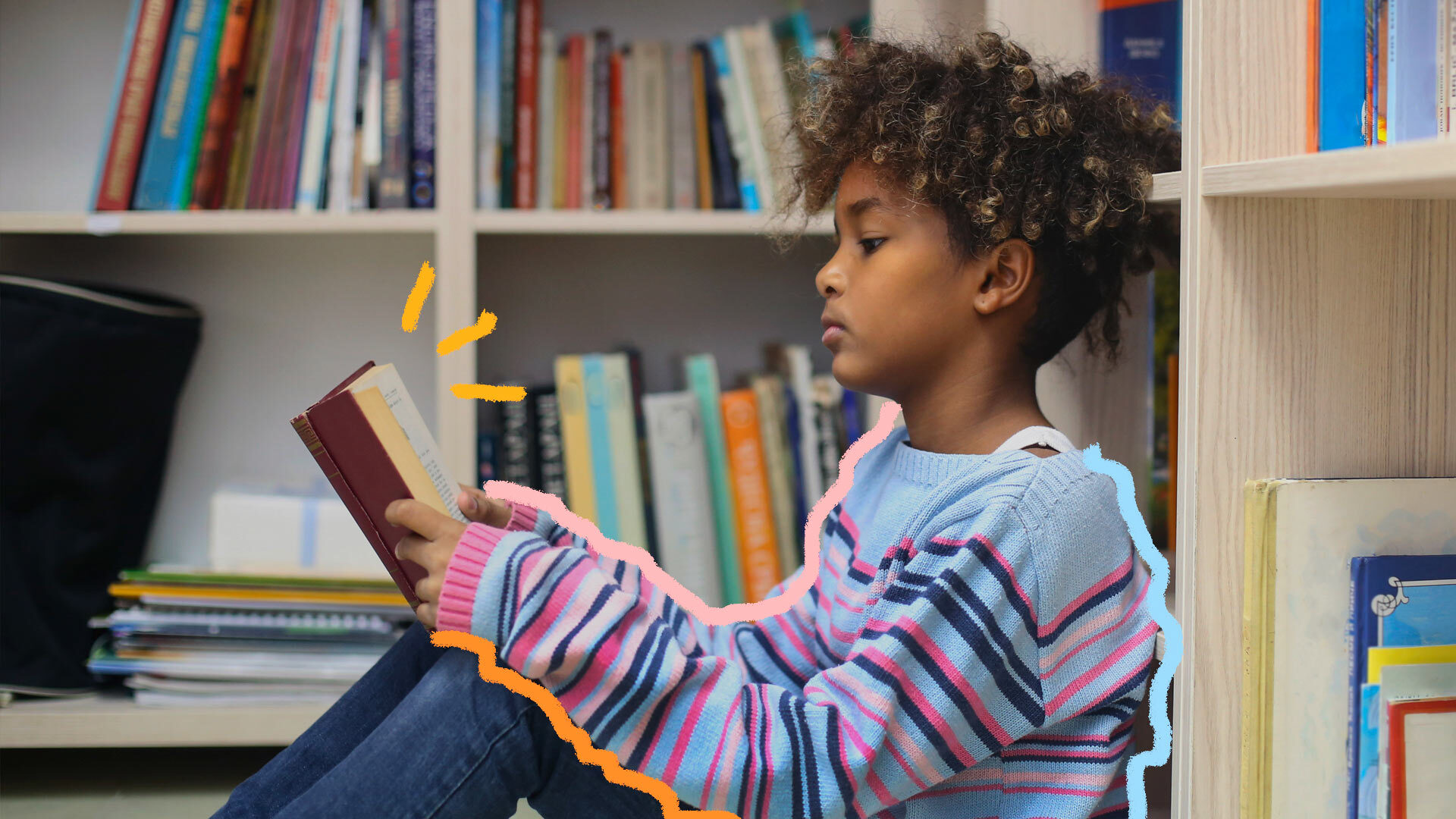 Na foto, uma menina lê um livro sentada no chão de uma biblioteca