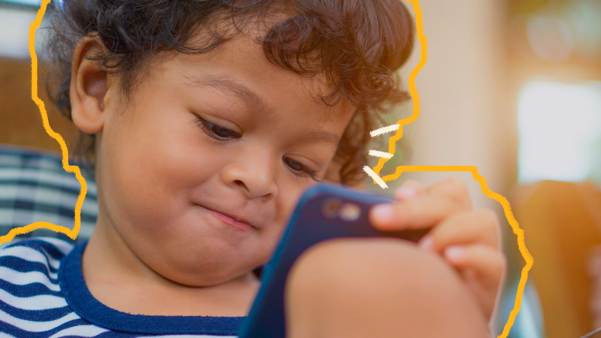 Um menino apoia um celular na perna e sorri para a tela enquanto acompanha algum conteúdo