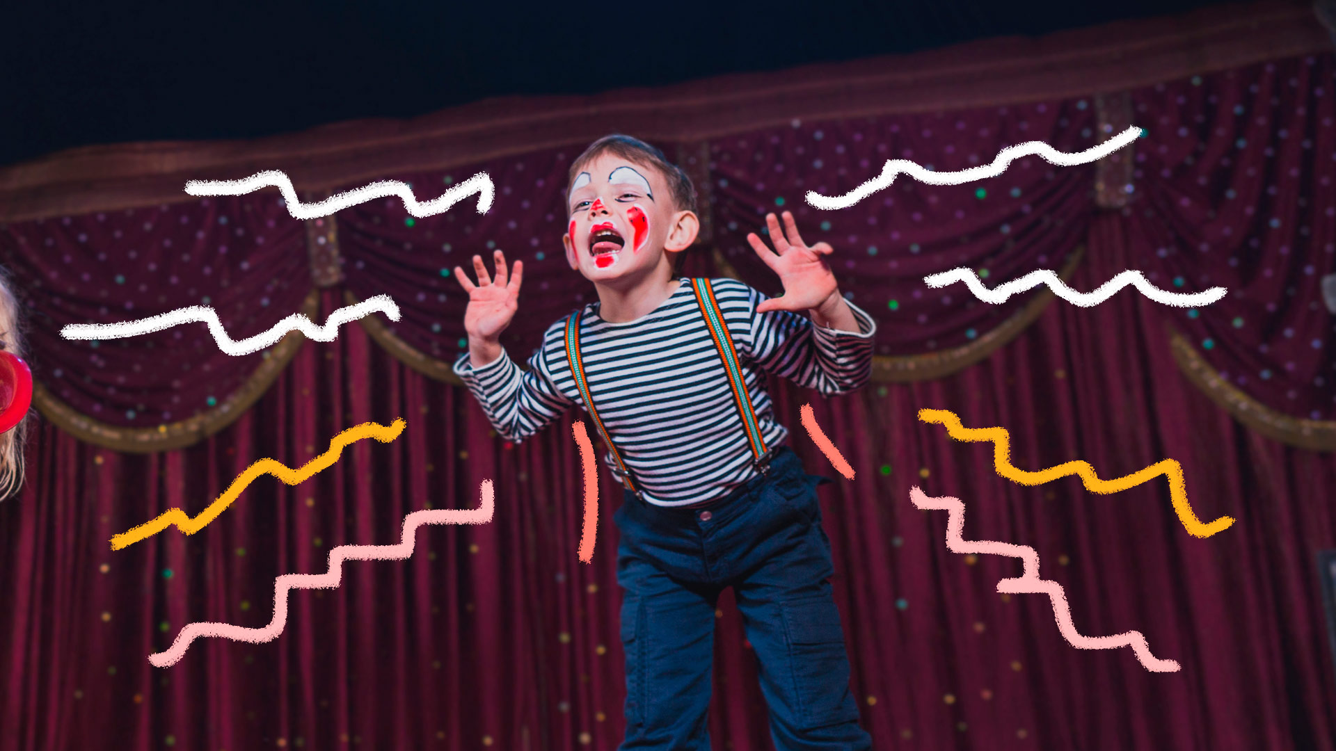 Um menino com roupas e maquiagem de palhaço está no palco. Atrás dele, ao fundo, uma cortina vermelha típica de teatro