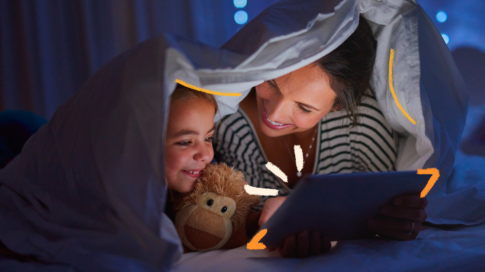 Mãe e filha olham sorridentes para um tablet, com um lençol acima delas