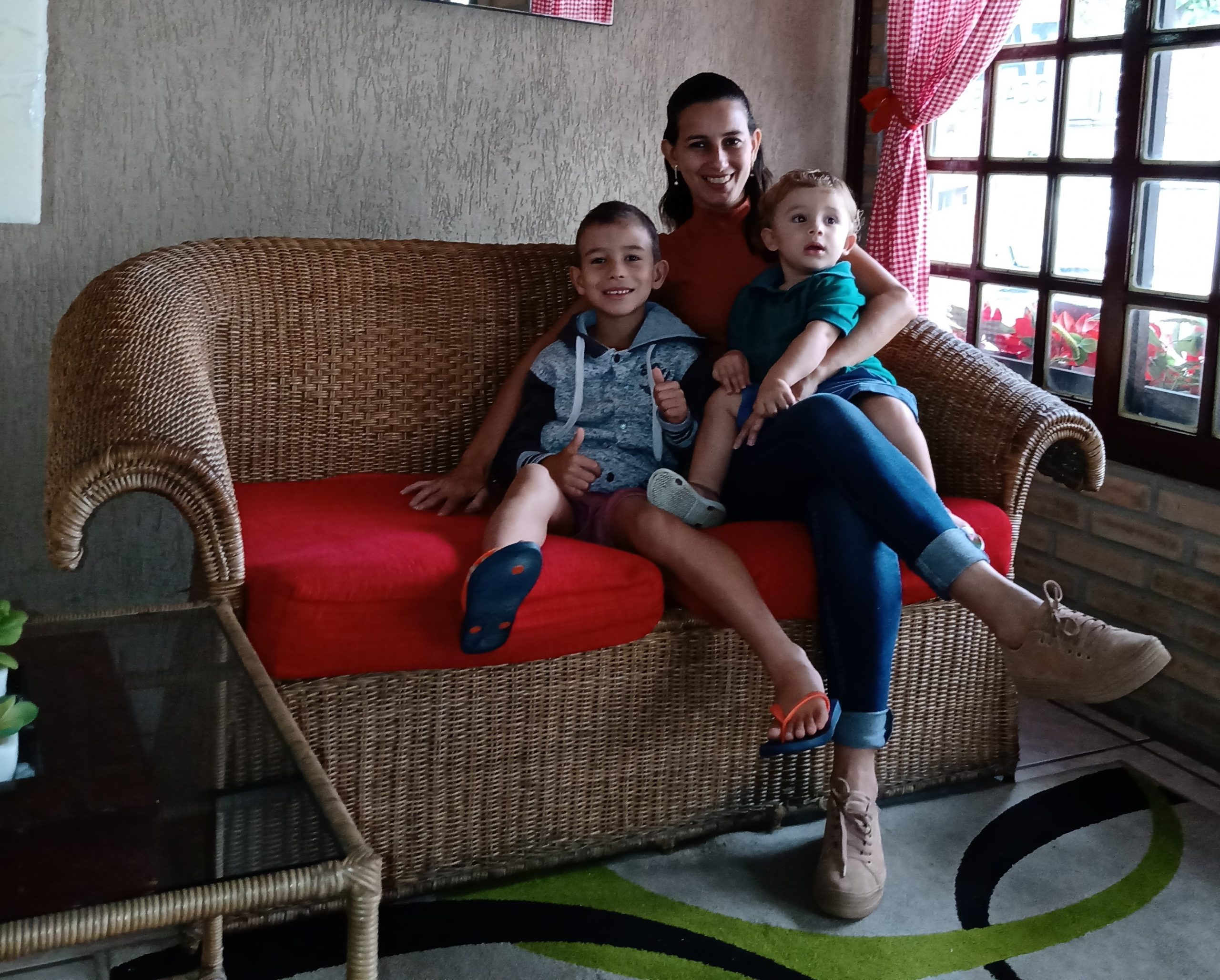 Uma mulher de cabelos presos e amarrados, sentada em um sofá com duas crianças no colo