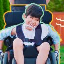 Criança sorrindo em uma cadeira de rodos e um aparelho ortodôntico externo à boca