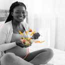 Alimentação na gravidez: foto em preto e branco de uma mulher grávida segurando um bowl com legumes (estes, coloridos) e sorrindo