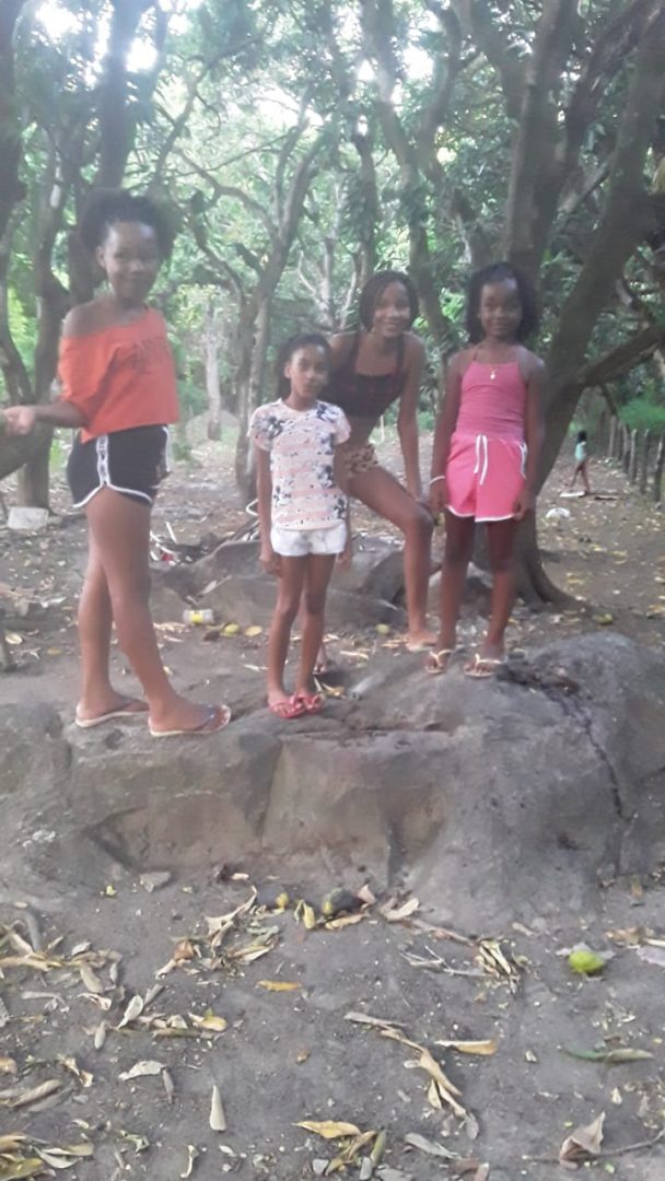 Quatro meninas quilombolas, vestindo shorts e camiseta, fazem uma 'pose', em meio a uma mata.