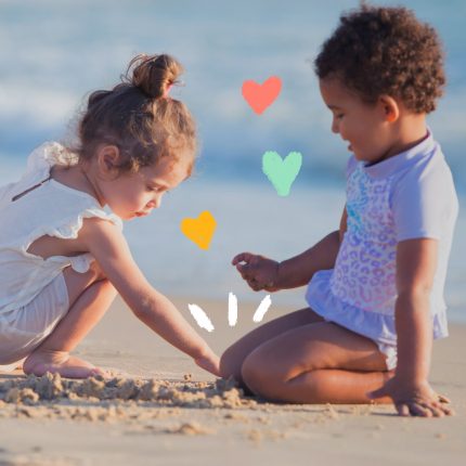 Duas meninas pequenas brincam na areia com o mar ao fundo