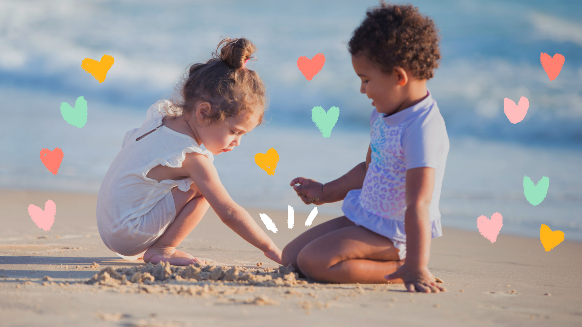 Duas meninas pequenas brincam na areia com o mar ao fundo