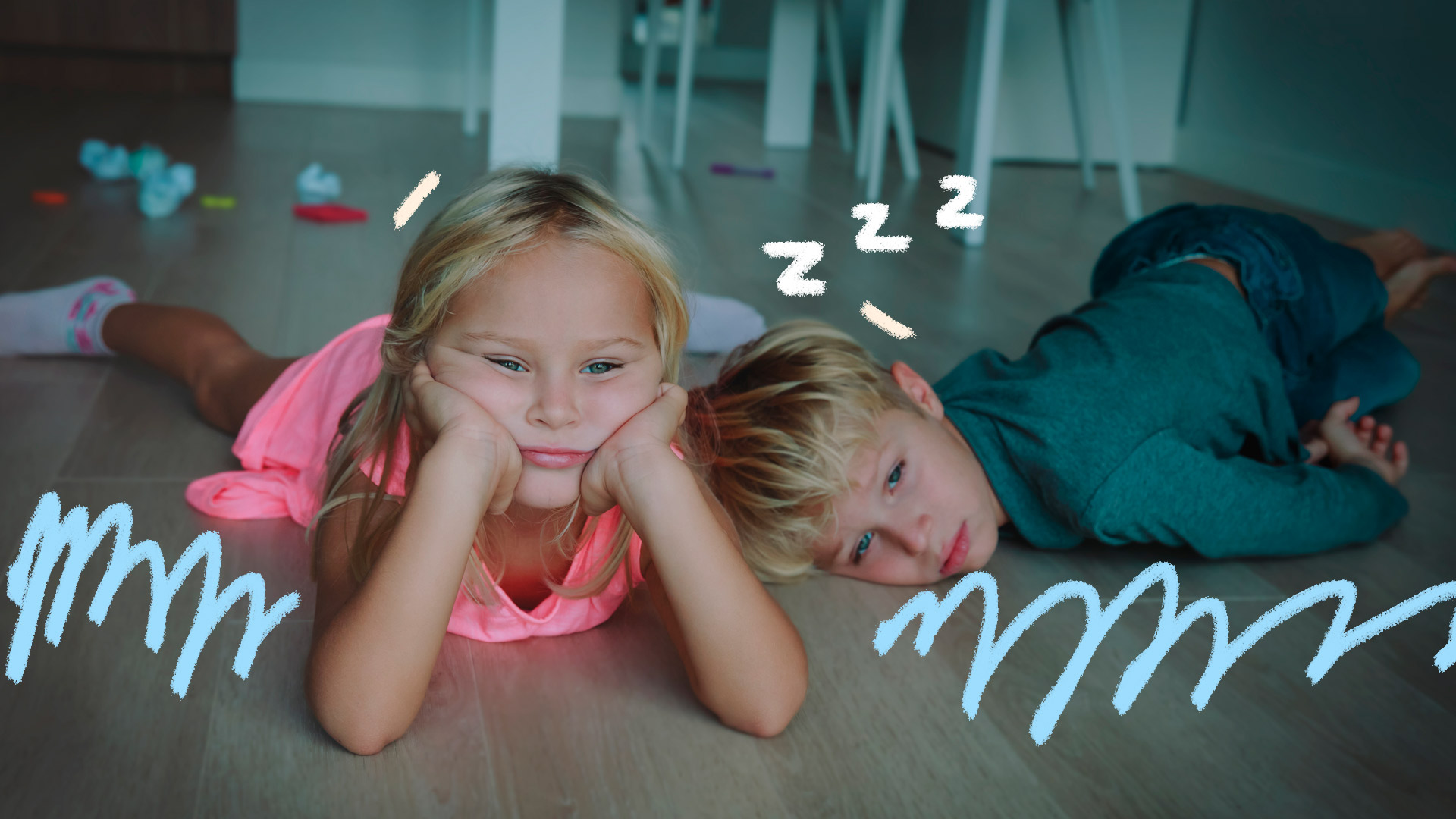 Um menino e uma menina ambos loirinhos, estão deitados no chão com cara de entediados.