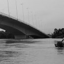 Enchente no Acre: foto em preto e branco de um barco em lugar alagado, com uma ponte ao fundo