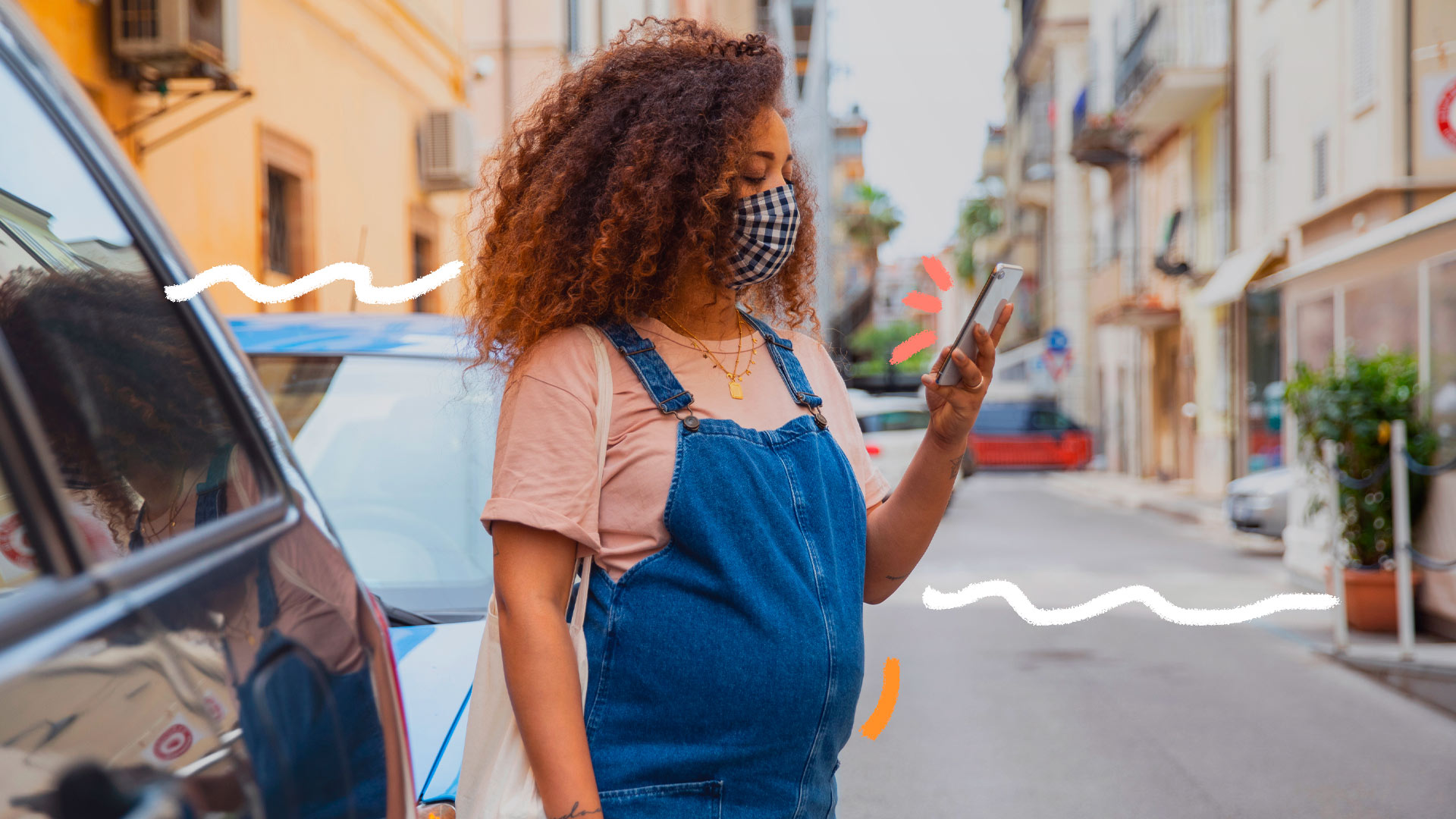 Foto de uma mulher grávida na rua, usando máscara e olhando para o celular