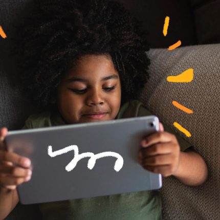 Uma menina está deitada no sofá e segura um tablet com as duas mãos