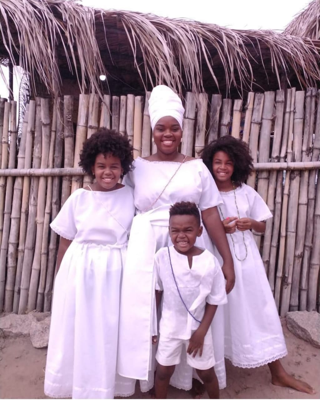 Uma mulher negra vestida de branco com seus três filhos (duas meninas e um menino), todos também vestidos de branco