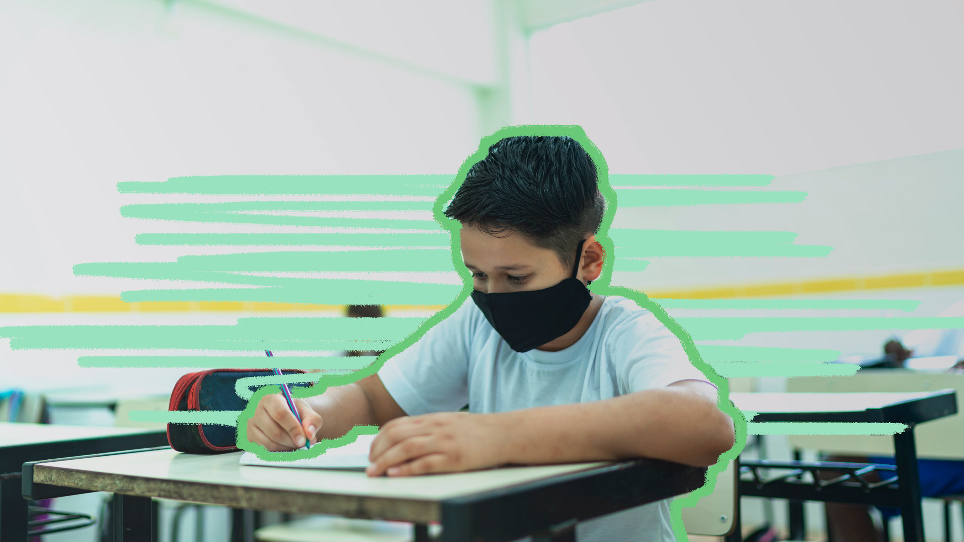 Foto de um menino em uma sala de aula praticamente vazia. Ele usa máscara e ocupa a sua carteira