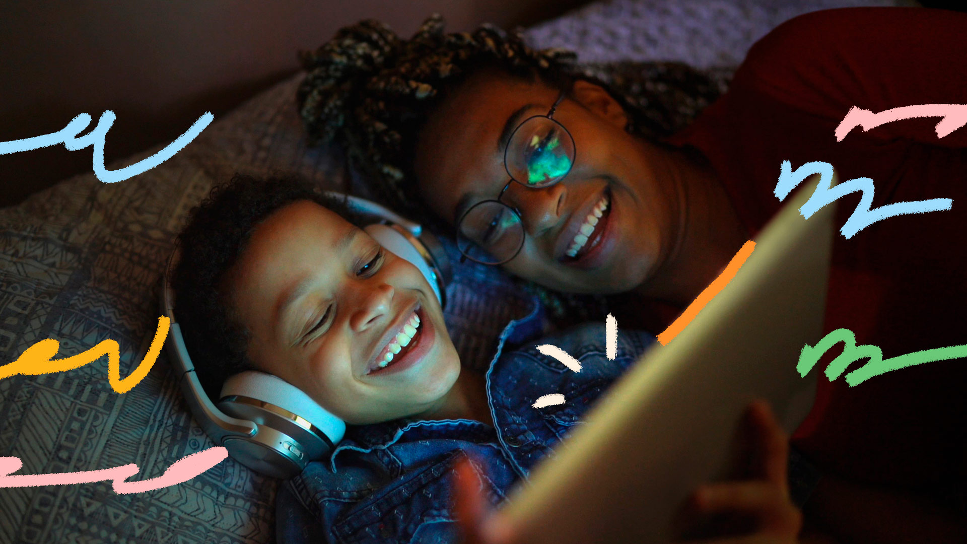 Aplicativos de contação de histórias: Uma mulher e um menino, ambos de pele negra, estão assistindo a algo no tablet e rindo